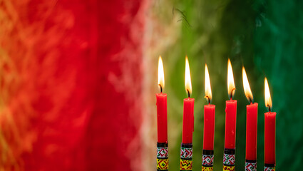 Seven red candles burning brightly on a kwanzaa kinara with a colorful background