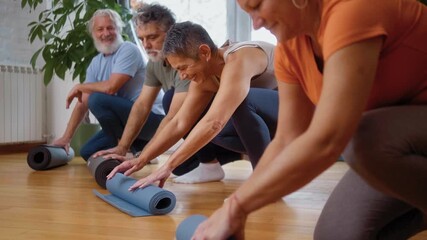 Group of active seniors smiling as they roll up their yoga mats after a fitness class, showing teamwork, healthy aging, and a positive wellness routine in a friendly studio atmosphere. - Powered by Adobe