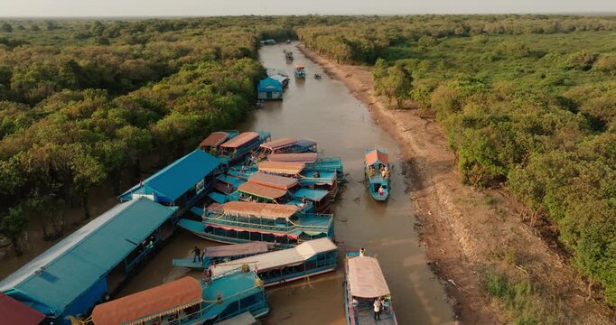 Tour boats docked along a muddy river near Tonle Sap floating village in Cambodia