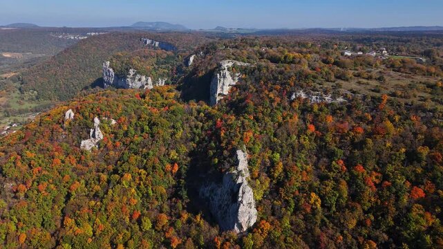 Aerial perspective of Cirque du fer a cheval in France featuring rugged limestone cliffs rising above dense autumn forest and rolling hills, highlighting vivid seasonal colors and dramatic terrain