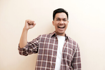 Fototapeta premium Southeast Asian man wearing flannel shirt showing happy excited expression with clenched fist, on white isolated background.