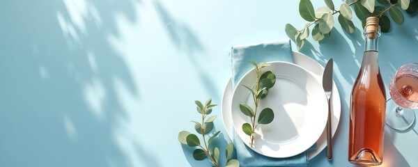 Spring holiday table with rose wine bottle, eucalyptus leaves, and white plate setting on blue background. Romantic outdoor meal arrangement with natural light and shadows.