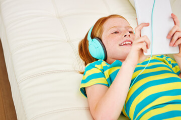 Headphones, smile and kid on couch with tablet, audio and cartoon streaming on video app. Happy, digital and child at house with tech, music subscription or watching series on entertainment platform.