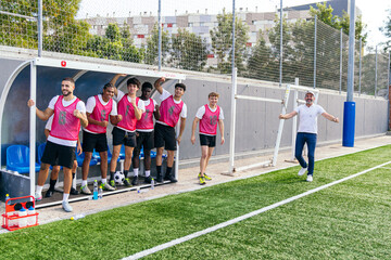 Football players and coach celebrating a goal from the sideline bench during a soccer match. Happiness and team spirit