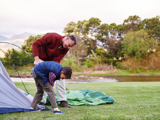Father, boy and building tent by river, camping and happy with help, support or teaching in nature. People, dad and son with shelter, campsite or smile for learning survival skills on family vacation