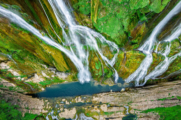 Aerial view of spectacular waterfall flowing over layered rocks into a deep blue river pool.