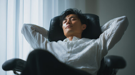 Japanese man leaning back for a posture break in an ergonomic office setup. Calm workplace wellness moment in a contemporary environment. Businessman in office chair, taking short break. Asian man.