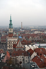 Fototapeta premium Aerial view of Poznań Town Hall and surrounding historic buildings with red rooftops and foggy skyline.