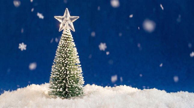 Snowy miniature evergreen christmas tree with glowing star topper standing in winter snow against deep blue background and falling snowflakes - Powered by Adobe