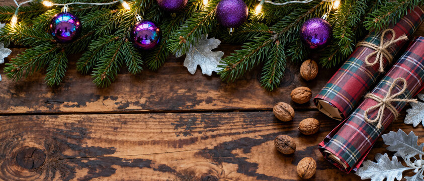 Festive christmas border with purple baubles, fir branches, crackers, walnuts and silver leaves on rustic wooden background - Powered by Adobe