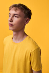 Fototapeta premium Yellow shirted male model with calm expression stands against a matching yellow backdrop, soft lighting highlights color harmony and minimalist studio composition