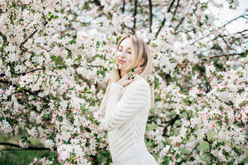 Blonde woman enjoying spring blossoms, peaceful moment in blooming cherry garden, seasonal beauty, floral fashion concept, nature appreciation, feminine serenity, romantic outdoor lifestyle