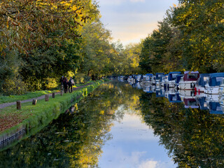 River Wey Navigation with moored boats and people enjoying the towpath on a calm autumn day near Byfleet and New Haw in Surrey