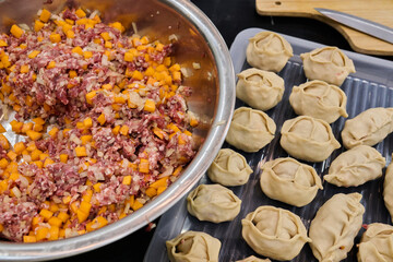 Freshly prepared meat and vegetable filling in a bowl beside neatly shaped dumplings on a tray, showcasing culinary creativity and preparation process