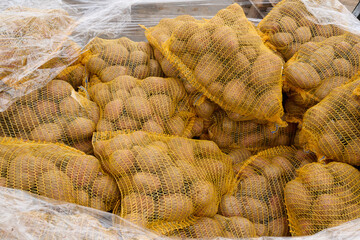Freshly harvested potatoes in yellow mesh bags stacked together, showcasing agricultural produce and vibrant textures in a rustic setting