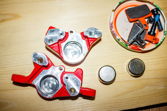 Bright red bicycle brake calipers split open for maintenance on a light wooden surface, showcasing internal metal pistons and loose pads for repair or cleaning