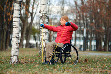 Man in wheelchair exercises with resistance bands in a park on a cool autumn day
