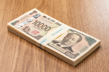 木目テーブルに置かれた百万円の一万円札束が象徴する日本円の高額資金