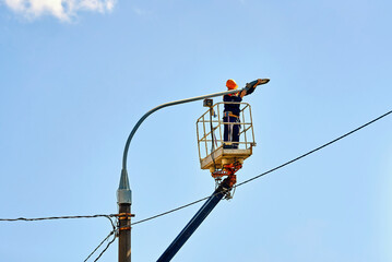 Worker in helmet and safety harness uses crane lift to install led street lamp during outdoor maintenance, safe and efficient city infrastructure lighting system service and repair. Electrician repair