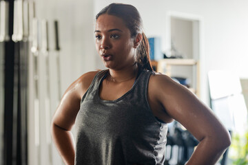 Woman catching breath wearing grey tank top in gym strength area near weight racks and dumbbells