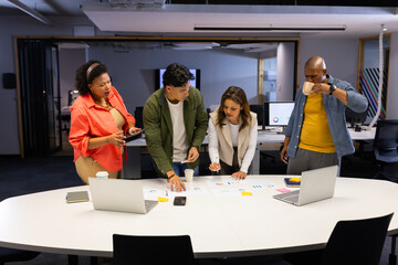 Diverse coworkers reviewing charts around conference table in office with laptops and coffee mugs
