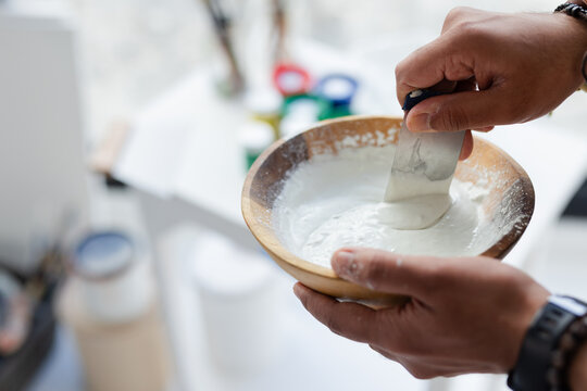 Indian adult male's hands scraping paste using spatula in wooden bowl at art studio, copy space