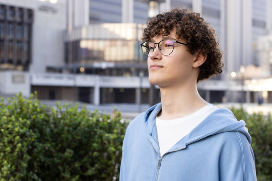 Man standing near green shrubs at office building wearing round eyeglasses and hoodie, copy space