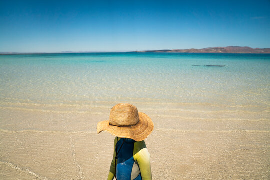 A young girl in a sun hat on beach at a clear sea