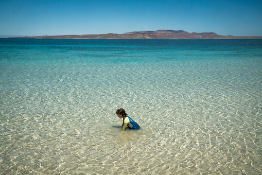 A young girl plays in a shallow, clear sea