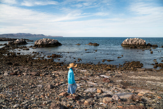 A young girl in sun hat walks on rocky desert beach