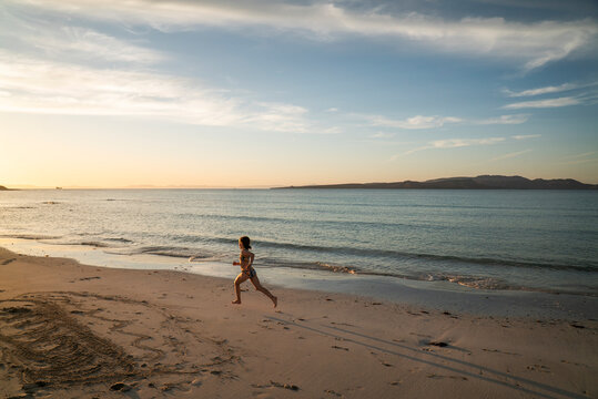A young girl runs down the beach at sunset.