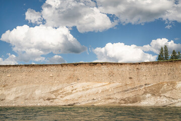 Striated layers of a river bank under blue skies and clouds