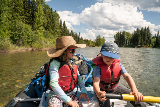 A young boy and young girl row a raft down a clear river.