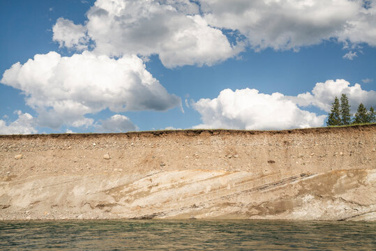 Striated layers of a river bank under blue skies and clouds