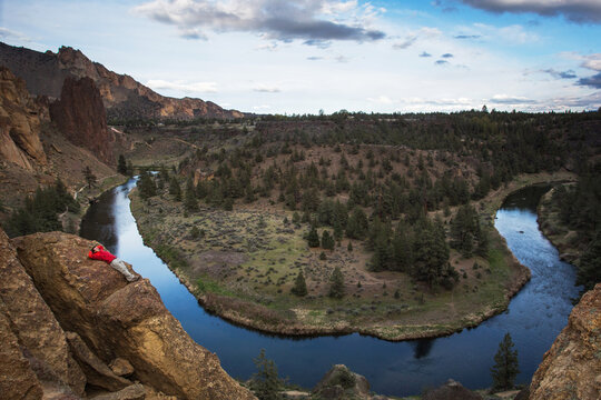 A man lies on a large rock overlooking a big bend in a desert river