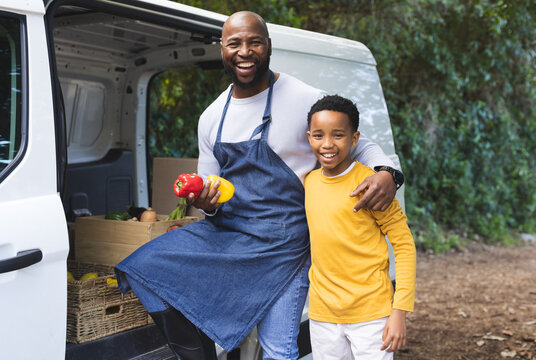 African American father and son sitting on edge of van holding bell peppers by wooden crates
