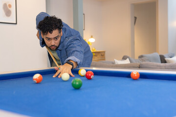 Man leaning over pool table lining up shot with cue stick amid billiard balls at home