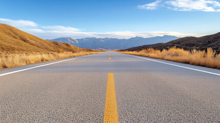 Open road desert landscape with distant mountains and golden grass under blue sky