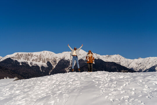 Mountains Snow Winter: Two women joyfully celebrate atop snowy peak, arms raised, bright sunny day. - Powered by Adobe