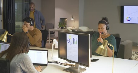 Diverse coworkers at desk using headsets and typing on laptop after getting printed files for calls - Powered by Adobe