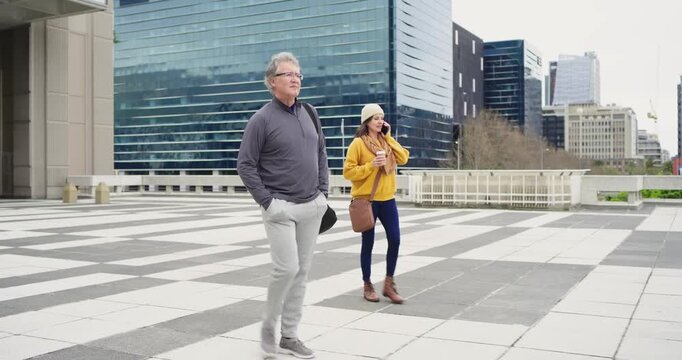 Spotting skyline man walking across plaza while woman following using smartphone and sipping coffee