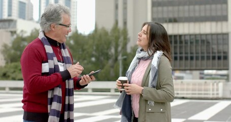 Diverse coworkers finishing call, tapping smartphone screen to show schedule on rooftop platform - Powered by Adobe