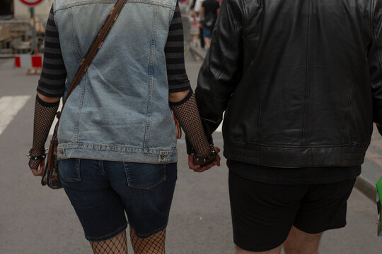 couple holding hands walking away together, denim vest and leather jacket pairing, fishnet stockings - Powered by Adobe