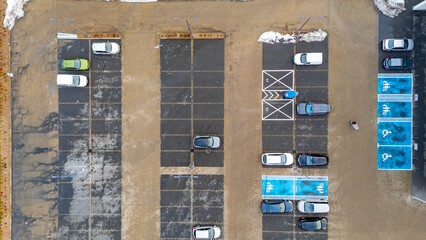 Aerial view of a parking lot with marked spaces, cars, disabled zones, EV spots and winter traces on the pavement
