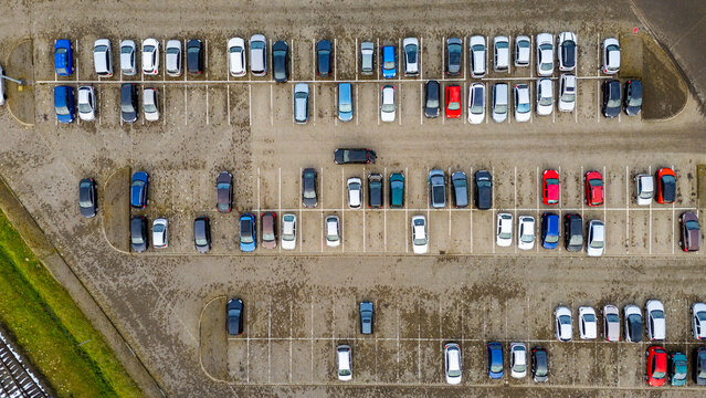 Aerial view of a crowded parking lot with parked cars, marked spaces, winter pavement texture and a parallel layout of parking rows