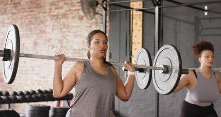 Upon barbell settling, diverse female friends bracing cores, squatting to tone legs by squat rack - Powered by Adobe