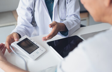 Close up, doctor examining a male patient's heart rate and measuring blood pressure with a blood pressure machine monitor in checkup at hospital or medical clinic.