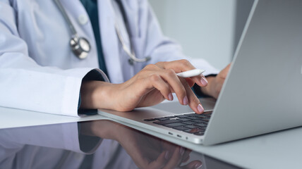 Doctor working in office, using laptop computer to access patient records on an EHR system. Medical student, female doctor using modern technology in practice for medical research, close up