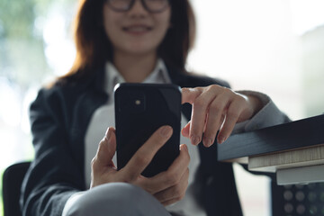 Smiling business woman sitting at table, using smartphone in office. Happy mature professional businesswoman hand holding mobile phone. Social media, internet networking, corporate business, close up