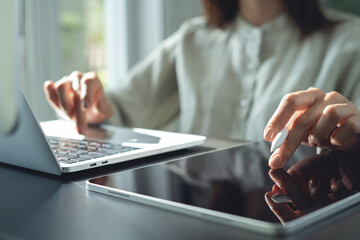 Closeup, business woman using digital tablet, finger touching on screen, working with laptop computer on office desk. Graphic designer using graphic tablet designing creative project